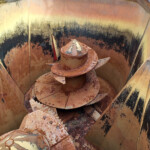 Rusty spiral auger inside a weathered yellow-brown industrial housing, with peeling paint and rust stains about the walls.