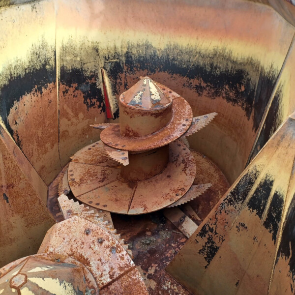 Rusty spiral auger inside a weathered yellow-brown industrial housing, with peeling paint and rust stains about the walls.