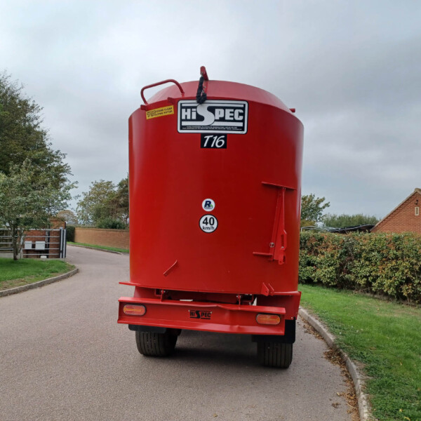Red Hi-Spec tanker trailer parked on a residential street with greenery and a brick house in the background, under a cloudy sky.