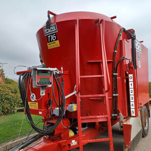 Red industrial tanker trailer with multiple hoses and a side-mounted control panel and safety stickers visible.