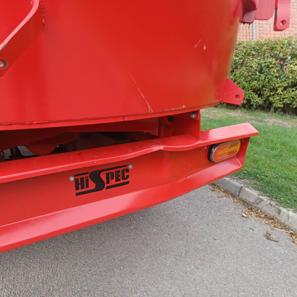 Close-up of a red industrial trailer panel with the Hi SPEC branding, showing a curved surface, mounting brackets and a few scratches by a curb and hedge.