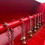 Red industrial machinery with multiple metal chains hanging along a red rail or beam.
