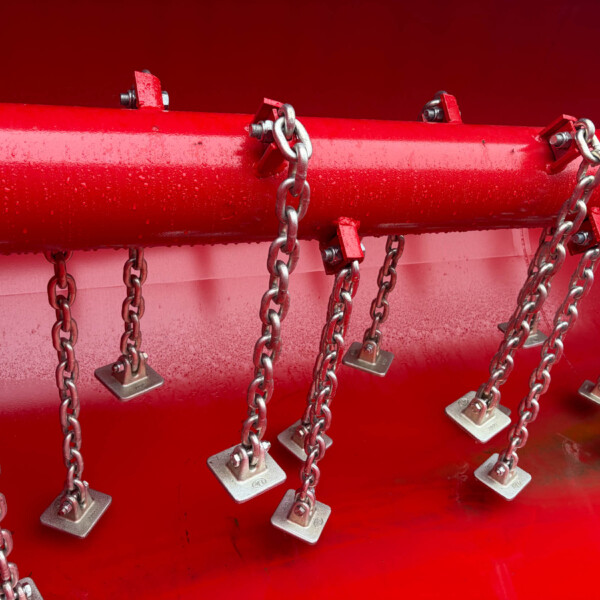 Red metal pipe with multiple chains and metal padlocks hanging along its length against a red background in an industrial scene.