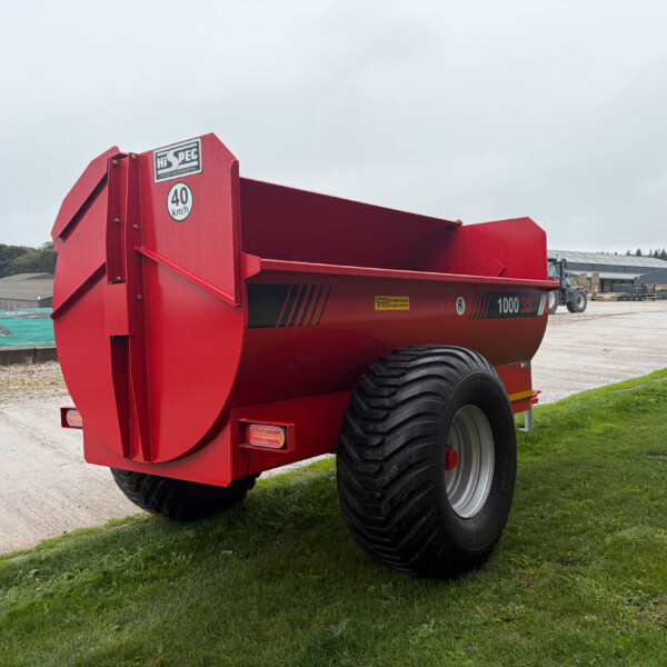 Red agricultural trailer with oversized rear wheels parked in a yard; a '40 km/h' sign and HiSPEC sticker are visible on its side.