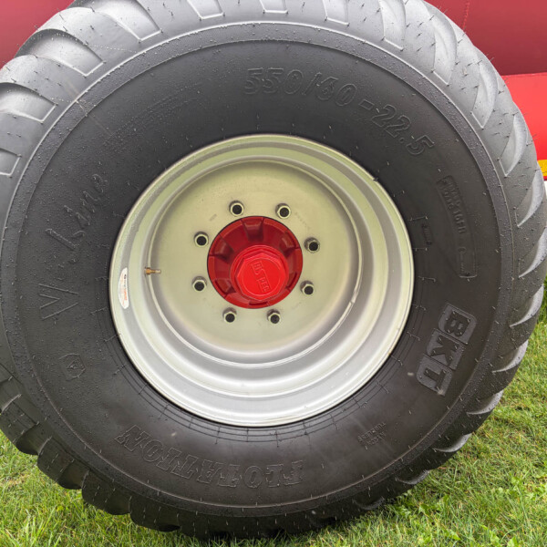 Close-up of a large tractor tire with a red hub, resting on a grassy field with part of red farm equipment in the background.