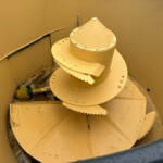 Yellow industrial auger (screw conveyor) with large helical blades inside a cylindrical housing, likely used to move bulk material.