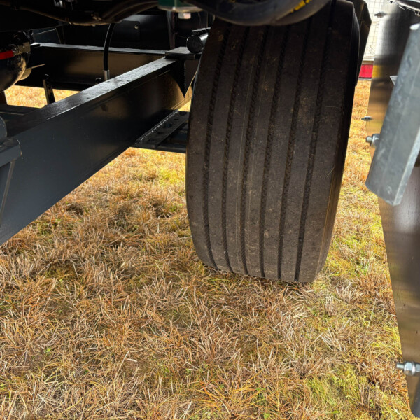 View under a heavy metal chassis with a large ribbed tire and steel frame, parked on dry grass.