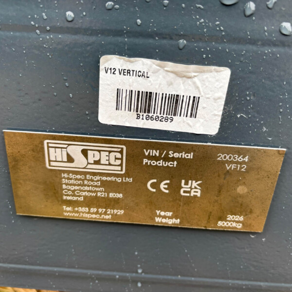White barcode label reading 'V12 VERTICAL' on a dark metal surface, above a gold manufacturer plate on an industrial device.