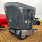 Close-up of a large gray grain trailer attached to a red truck at an outdoor machinery show, with vents and cables visible on the trailer.