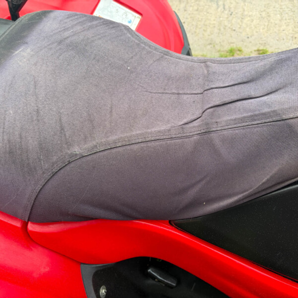 Close-up of a red motorcycle body with a black seat, featuring a small circular blue-and-white logo on the side.
