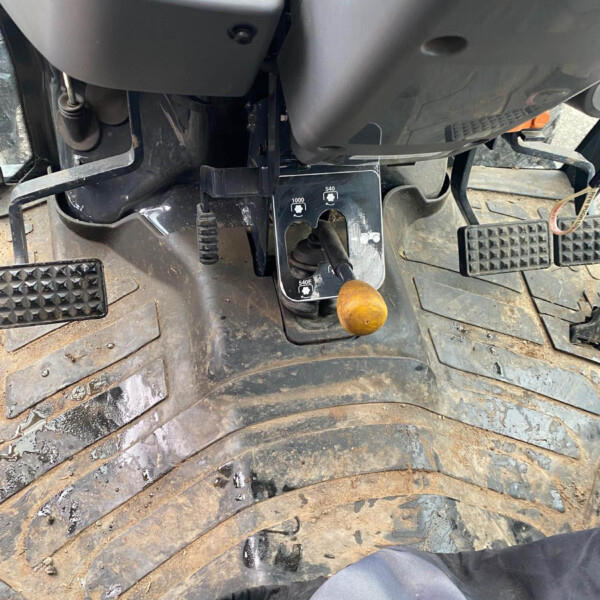Close-up of a muddy tractor cab floor showing the pedal area: accelerator/brake pedals and a gear selector with an orange knob