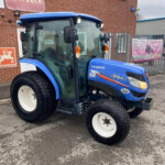 Front-right view of a blue Iseki TG 6370 tractor parked beside a brick building with a TORO sign above it.
