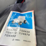 Open ISEKI tractor operator's manual with a blue cover showing a illustrated tractor, model numbers like TG6370 TG620, on a gray seat.
