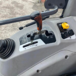 Close-up of a vehicle gear lever with a brown leather-wrapped handle and a yellow control knob, seen inside a cab with raindrop-covered windshield outside a brick wall.