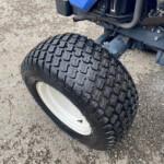 Close-up of a large off-road tire on a blue tractor, showing chunky tread and a white wheel rim on a gravel surface.