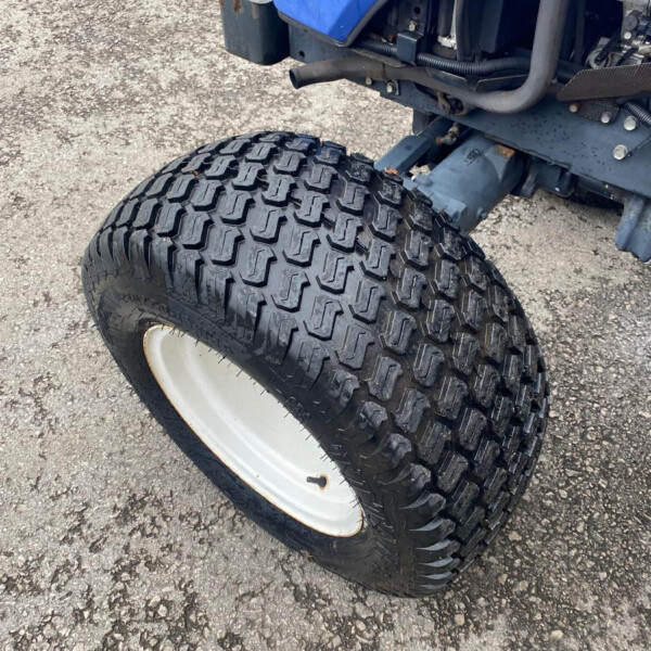Close-up of a large off-road tire on a blue tractor, showing chunky tread and a white wheel rim on a gravel surface.