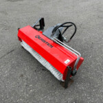 Red Kersten street-sweeper attachment with metal arms and white brush bristles on an asphalt surface