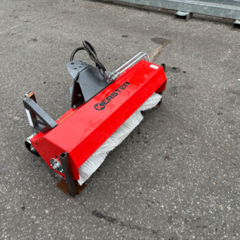 Red street-sweeper attachment with white bristle roller on a paved surface, showing metal mounting brackets.