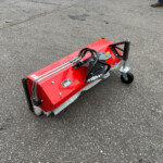 Close-up of a red street-sweeper attachment on asphalt with hydraulic hoses and a wheel visible at the edge.