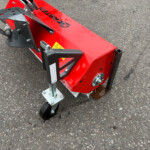 Red industrial equipment attachment with metal brackets and hoses on a wet asphalt surface.