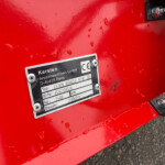 Close-up of red industrial equipment with a metal data plate attached, showing company name and model information, water droplets on the surface.
