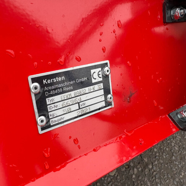 Close-up of red industrial equipment with a metal data plate attached, showing company name and model information, water droplets on the surface.