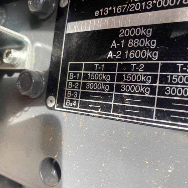 Close-up of a metal load-rating plate on industrial equipment showing capacities like 2000 kg and A-1 880 kg, A-2 1600 kg, with bolts nearby