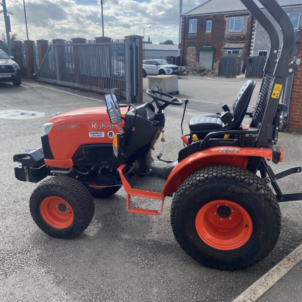 Orange Kubota tractor parked in a lot with a tall black gate and brick building in the background
