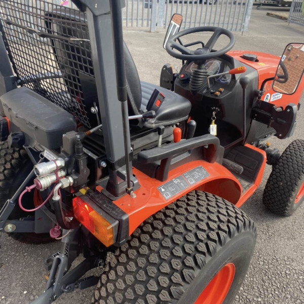 Close-up of a red/orange tractor showing the steering wheel, dashboard, and large treaded rear tires in a yard behind a fence