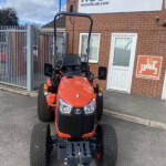 Front view of an orange Kubota tractor with a heavy front hitch parked outside a brick building with a Russell's sign.
