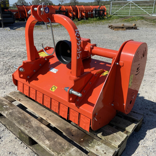 Orange industrial implement on a wooden pallet in a gravel lot, with other orange machines in background and a metal gate nearby.