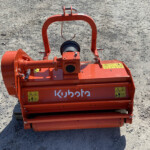Orange construction implement with cylindrical roller and metal frame on gravel, labeled Kubota, likely a compactor or mulch machine.
