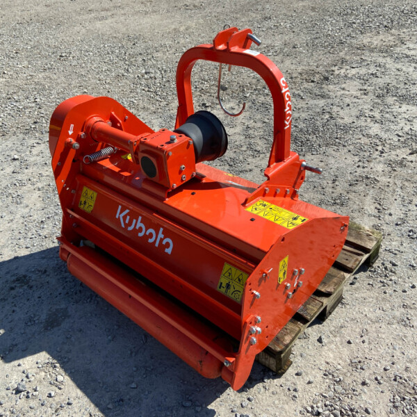 Orange Kubota wood chipper attachment on a pallet, outdoors on a gravel lot, with safety decals visible.
