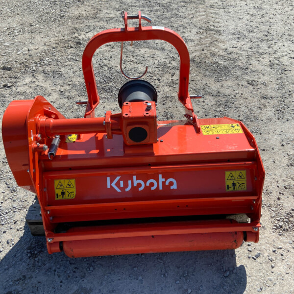 Orange Kubota agricultural implement viewed from above on a rocky surface, showing a curved frame, rotating drum, and warning labels.