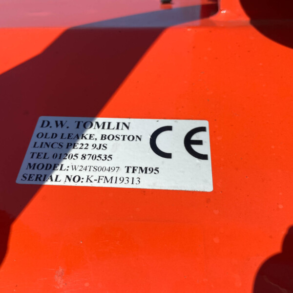 Close-up of a white label on an orange surface, showing manufacturer name 'D.W. TOMLIN' and model/serial information.