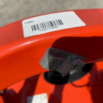 Barcode label on an orange metal frame, showing a printed UPC-style barcode and numbers.