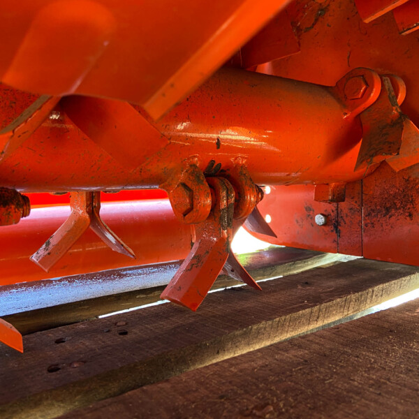 Close-up of orange-painted metal framework with bolts and sharp edges, part of heavy farming equipment on a wooden surface.