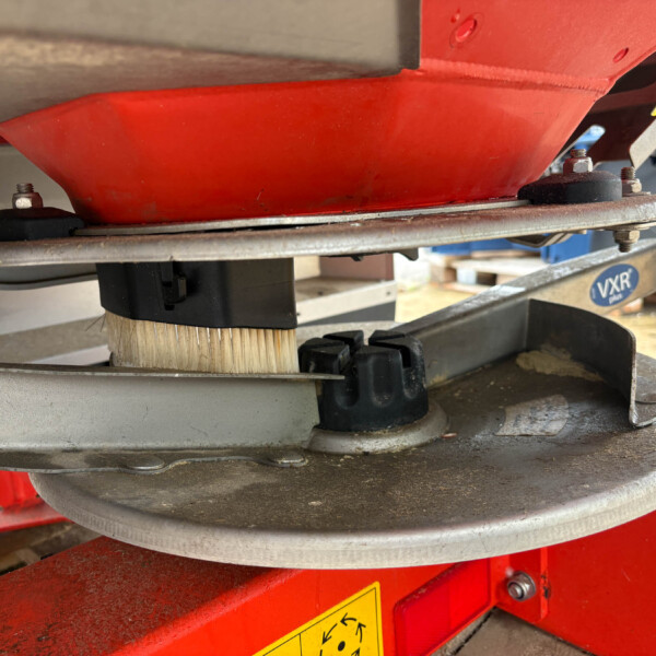 Close-up of a red industrial sanding machine with a circular abrasive wheel and a brush attachment, bolts and metal frame visible.