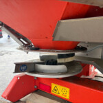 Close-up of a red industrial machine base with yellow warning icons and a STOP label, outdoors with a vehicle in the background.