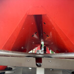 Interior view of a red metal industrial chute or housing with perforated panels and dark inner channel.