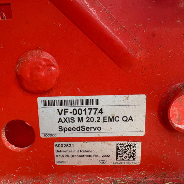 Close-up of a red metal surface with a barcode label reading 'VF-001774' and accompanying text, dirt and scratches visible around the label.