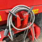 Coiled gray and black hoses hung on a red farm machine with warning stickers visible in the background, showing a dusty, rugged equipment setup.