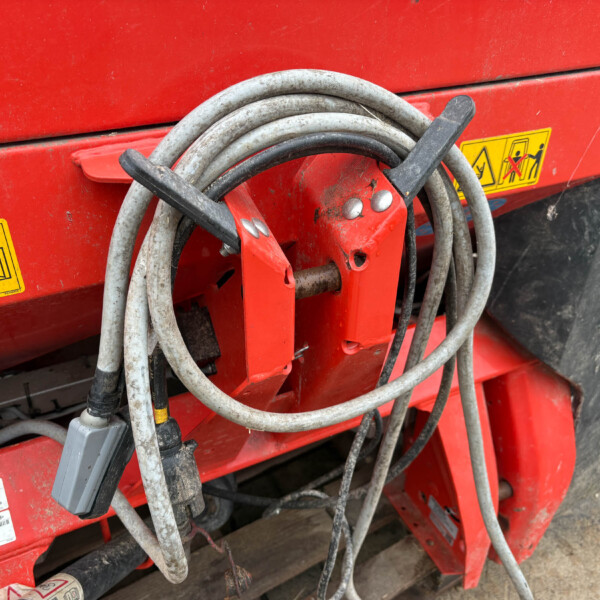 Coiled gray and black hoses hung on a red farm machine with warning stickers visible in the background, showing a dusty, rugged equipment setup.