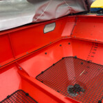 Red industrial hopper interior with a black wire-m mesh floor and a yellow bag tucked at the top edge.