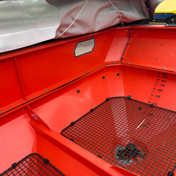 Red industrial hopper interior with a black wire-m mesh floor and a yellow bag tucked at the top edge.