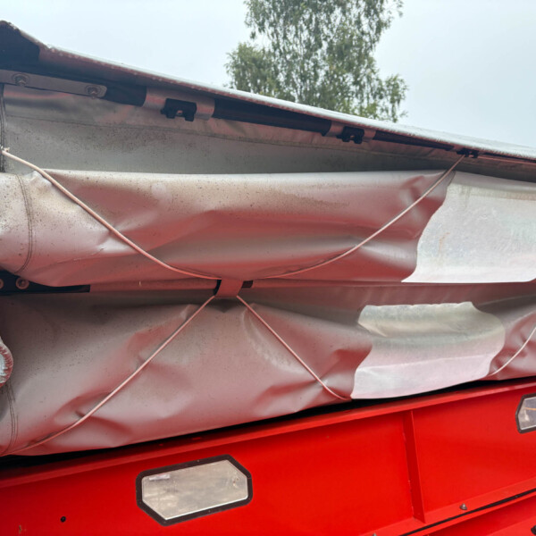 Close-up of a damaged red vehicle exterior with a torn gray cover, exposed wiring, and bent panels nearby.