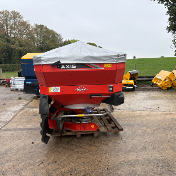 Red KUHN Axis farm implement with gray cover, parked on pallets in an outdoor yard