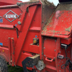 Red Kuhn Primor baler with hay debris on its surface, standing in a field; logo and model number visible (KUHN, Primor 3570 M).