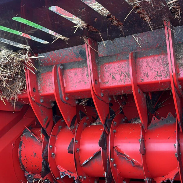 Close-up of red agricultural header with cutting blades and straw tangled between blades