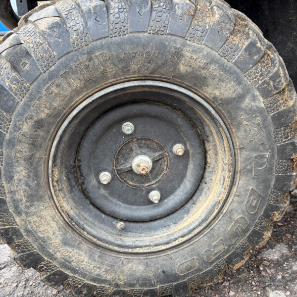 Close-up of a large muddy off-road tire on a wheel, with a blue car visible in the background